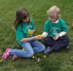 Two children sitting on the grass playing with a flower.