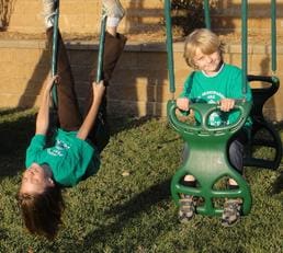 Two children on swings and a little boy sitting in the back.