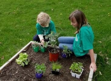 Two children are sitting in a garden with plants.