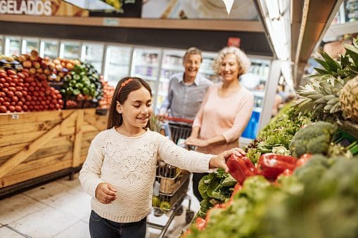 A girl is reaching for an apple in the produce section of a store.